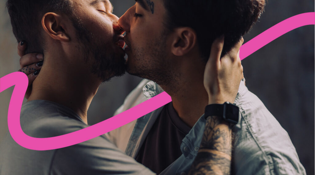 Two men kiss in a close embrace, conveying romantic affection with a pink decorative swoosh across the frame, not focusing on faces.